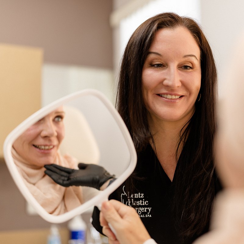 Sculptra 2 Aesthetic provider at Lentz Plastic Surgery & Medical Spa holding a mirror for a patient to review their facial treatment results.