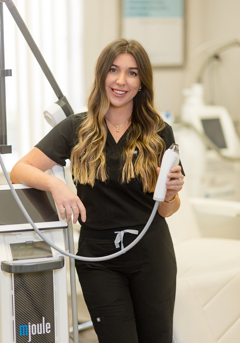 BBL HEROic 1 Professional aesthetician in black scrubs posing with a medical-grade laser treatment device at an aesthetic clinic.