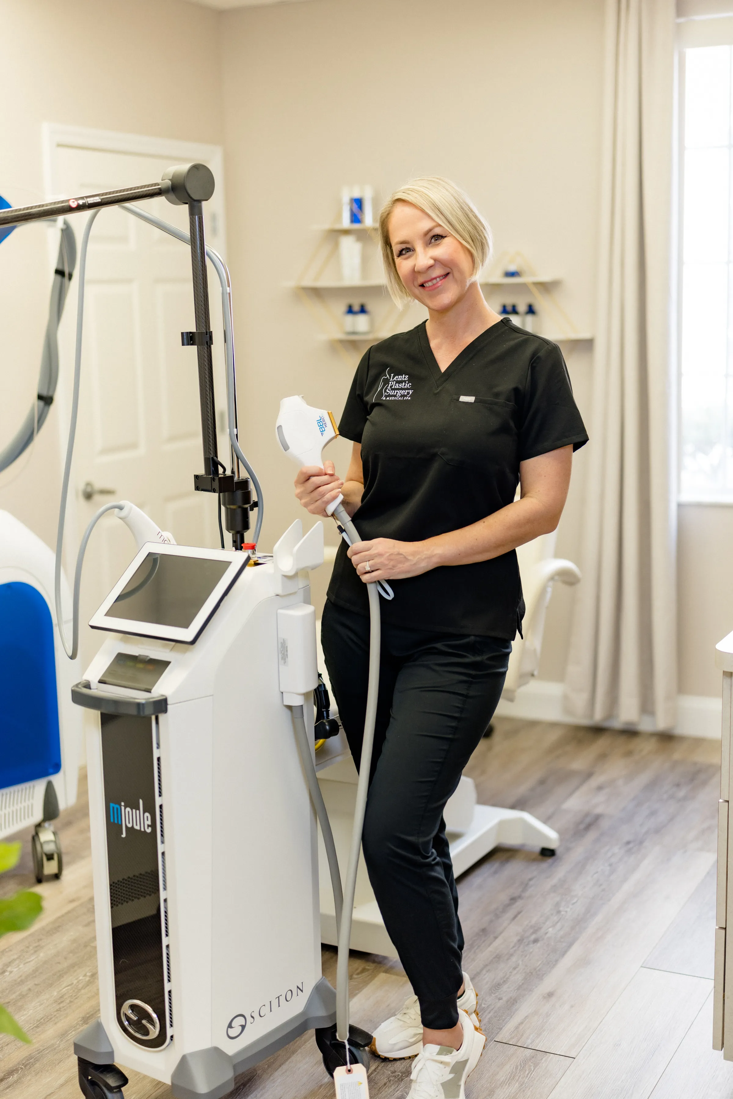 BBL HEROic 1 Judit Professional aesthetician in black scrubs posing with a medical-grade laser treatment device at an aesthetic clinic.